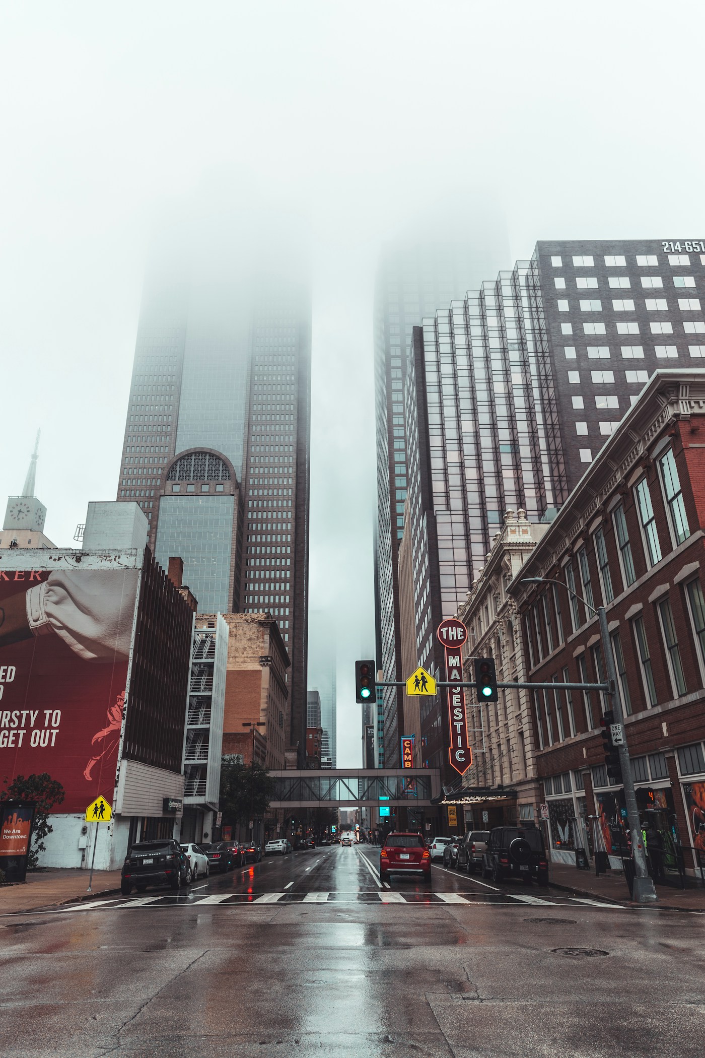 A foggy downtown Dallas street on a wet morning, skyscrapers disappearing into low cloud above the Majestic theatre marquee.